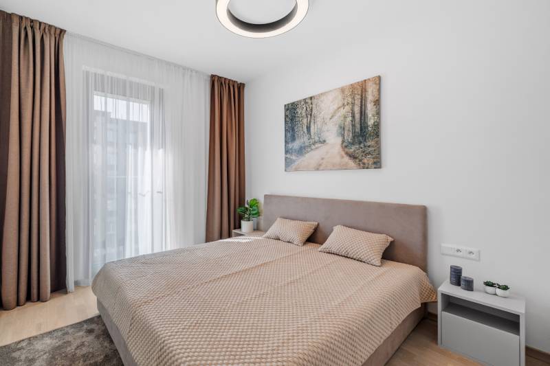 I Prenájom exkluzívneho 2-i bytu v projekte Metropolis - Spálňa s veľkou posteľou, závesmi a podlahou s dreveným dekorom v 2-izbovom byte.