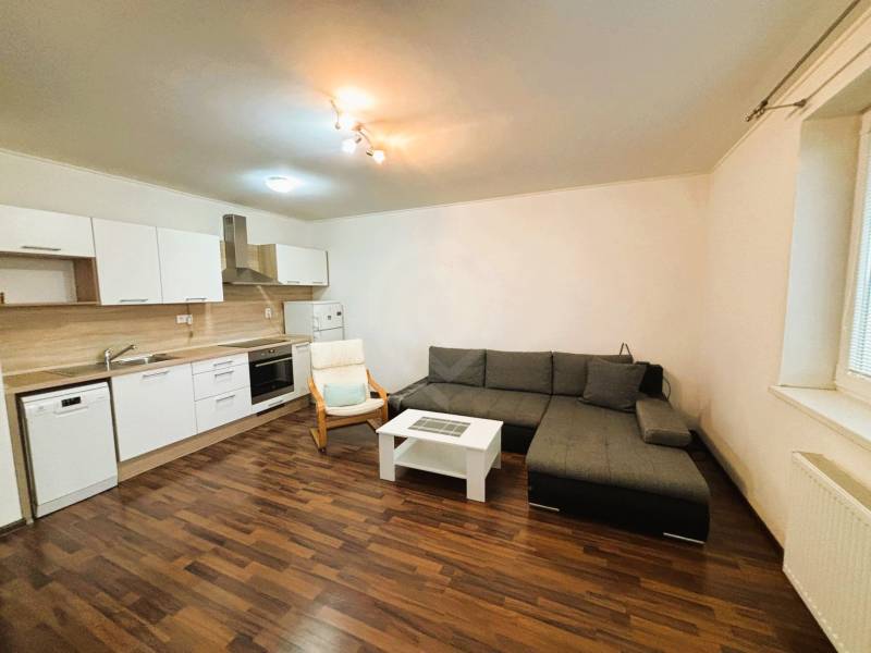 Prenájom 2 izbový byt – 52 m², lokalita – Malá Paka. - Obývacia izba v 2-izbovom byte s rohovo umiestnenou sedačkou a kuchynskou linkou.