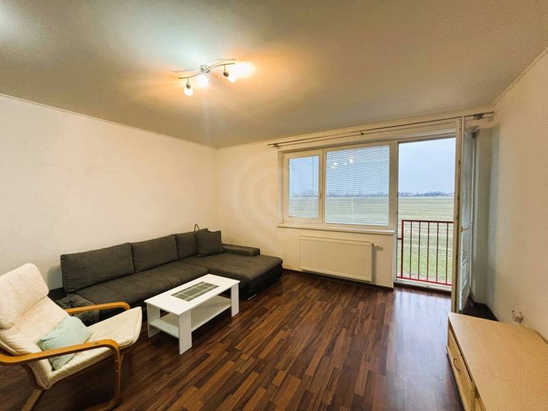 Prenájom 2 izbový byt – 52 m², lokalita – Malá Paka. - Obývacia izba v 2-izbovom byte s podlahou s dreveným dekorom a pohovkou.