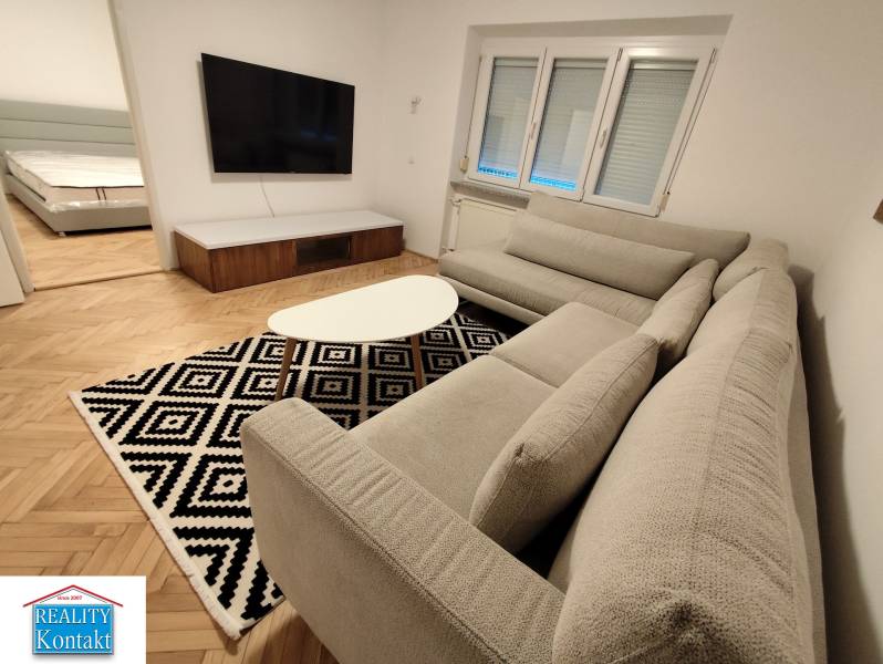 Na prenájom 2-izbový byt  Nové Zámky - Obývacia izba v 2-izbovom byte s veľkou TV a podlahou s dreveným dekorom.