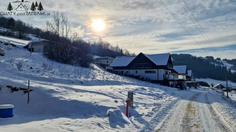 Stavebný pozemok s panoramatickým výhľadom Mýto Nízke Tatry - Zasnežená ulica v Mýto pod Ďumbierom s výhľadom na domy a okolitú krajinu.
