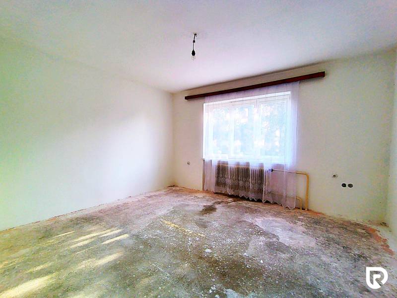 Rodinný dom v obci Borskom Mikuláš. - Prázdna izba v rodinnom dome s ošúchanou podlahou, radiatorom a závesmi.