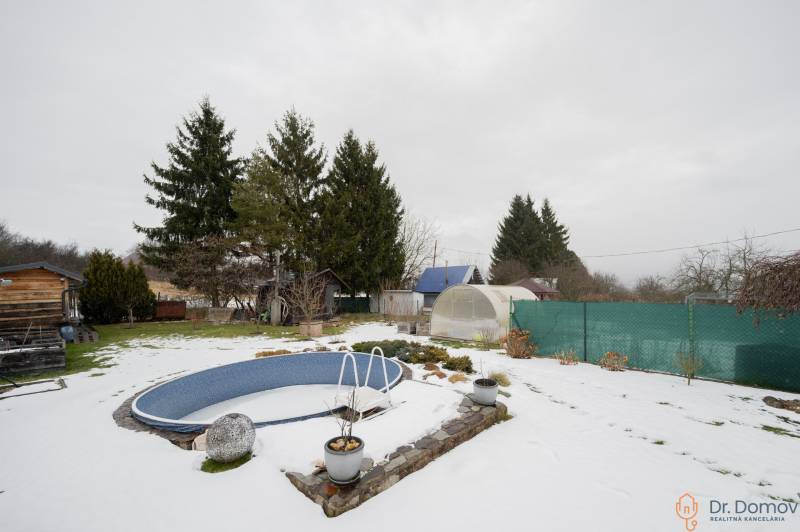 Záhradná chatka Handlová - Zasnežená záhrada pri chate v Handlovej s bazénom, skleníkmi a ihličnatými stromami.
