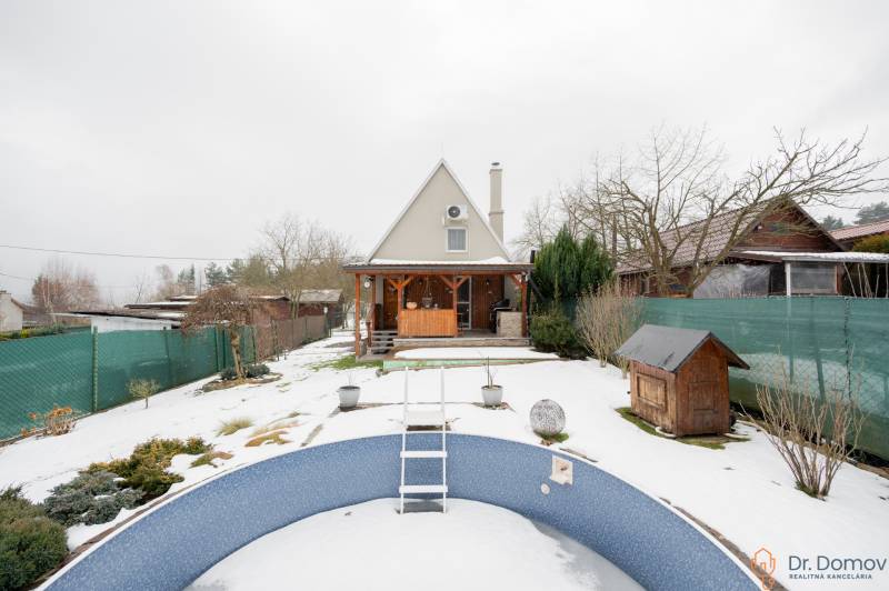 Záhradná chatka Handlová - Zasnežená záhrada s chatou v Handlovej a prázdnym bazénom v popredí.