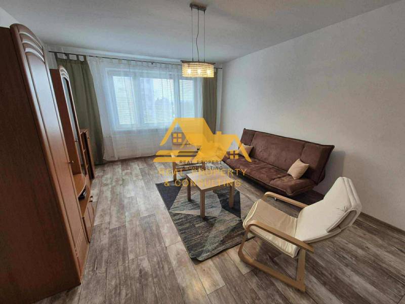 Prenajmem 3 izbový byt s loggiou v Nových Zámkoch - Obývačka v 3-izbovom byte s pohovkou, kreslom a podlahou s dreveným dekorom.