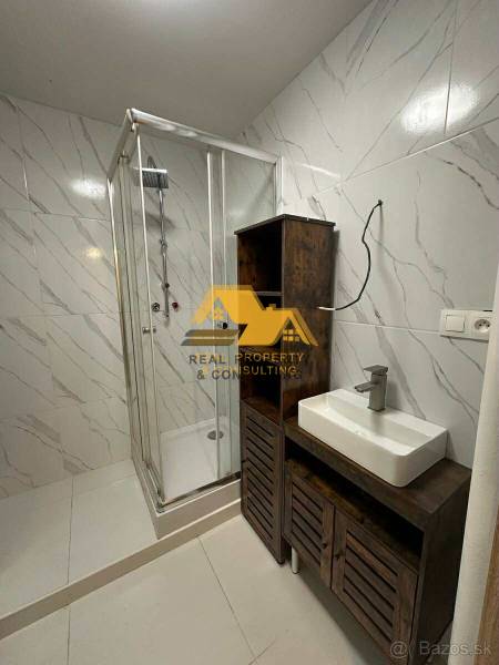 Prenajmem prerobený 2 izbový byt s balkónom v Nových Zámkoch - Kúpeľňa v 2-izbovom byte s bielymi dlaždicami, sprchovacím kútom a umývadlom na skrinke.