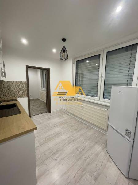 Prenajmem prerobený 1 izbový byt v Nových Zámkoch - Kuchyňa v 1-izbovom byte s podlahou s dreveným dekorom a bielymi elektrospotrebičmi.