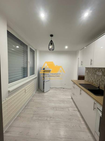 Prenajmem prerobený 1 izbový byt v Nových Zámkoch - Kuchyňa v 1-izbovom byte s podlahou s dreveným dekorom a moderným osvetlením.