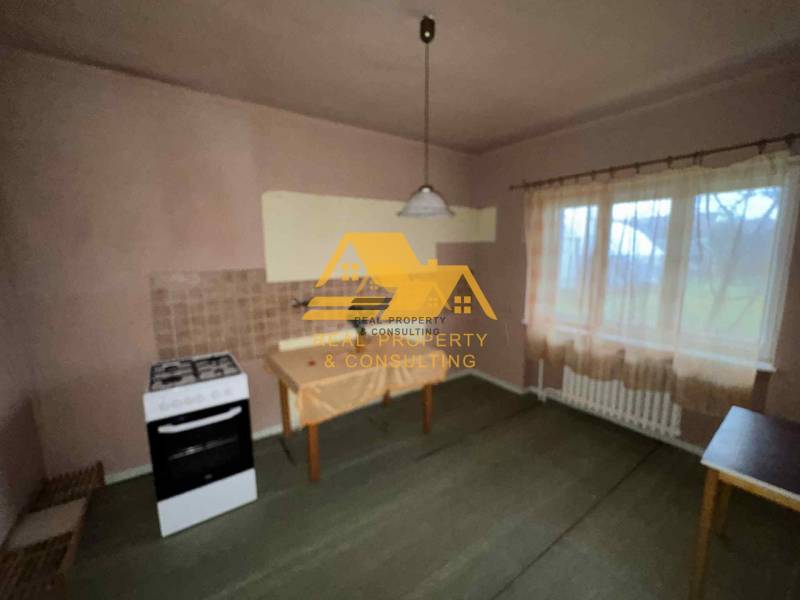 Predám rodinný dom s garážou v obci Dvory nad Žitavou - Kuchyňa v rodinnom dome so sporákom, stolom, záclonou a svetlom dekorom stien.