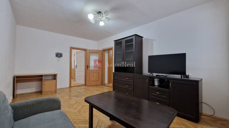 AstonReal:  predaj 2-izbový byt 54 m2, Poprad - Západ, Komenského - Obývacia izba s tmavým nábytkom a podlahou s dreveným dekorom v 2-izbovom byte.