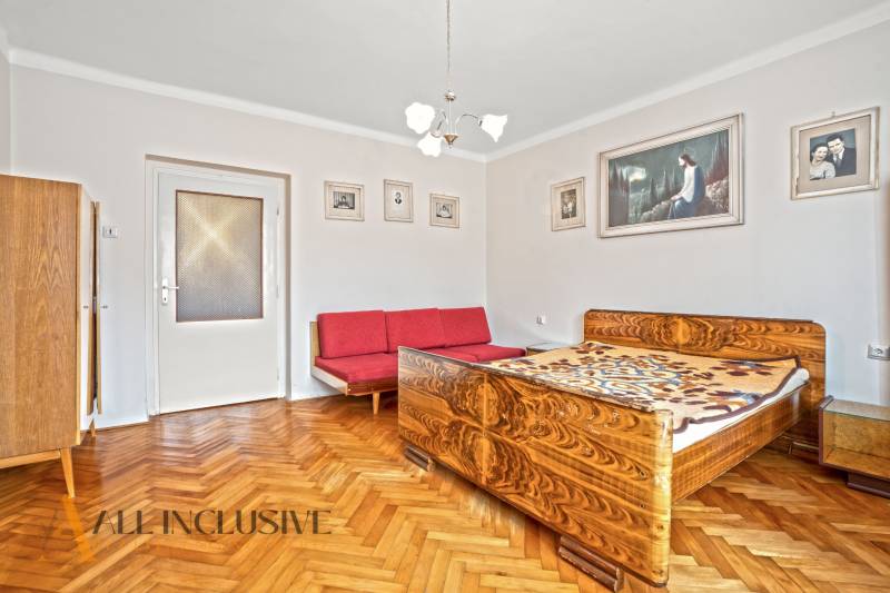 NA PREDAJ 4-IZBOVÝ RD NA VEĽKOM POZEMKU, VRAKÚŇ - Spálňa v rodinnom dome s posteľou, červenou pohovkou a podlahou s dreveným dekorom.