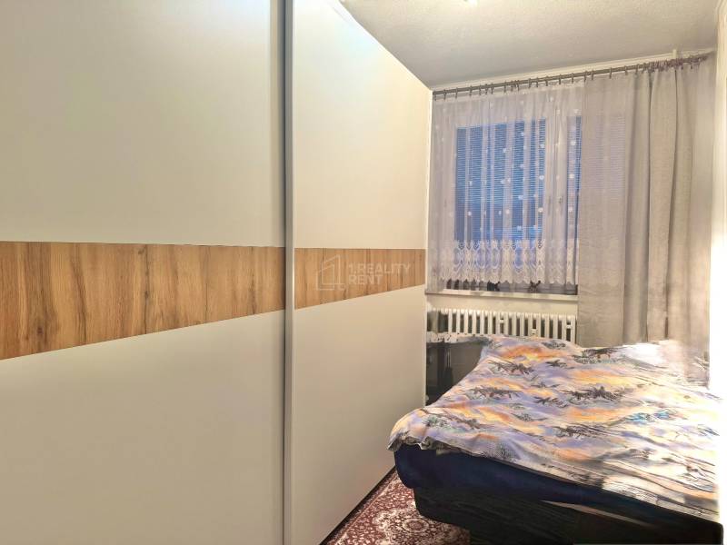 Predaj 2-izbového bytu v Krásne nad Kysucou - Spálňa v 2-izbovom byte s veľkou skriňou a oknom s dekoratívnymi závesmi.