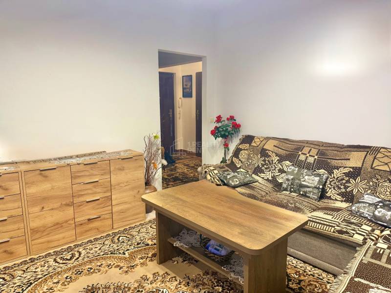 Predaj 2-izbového bytu v Krásne nad Kysucou - Obývacia izba v 2-izbovom byte s drevenou komodou a vzorovaným kobercom.