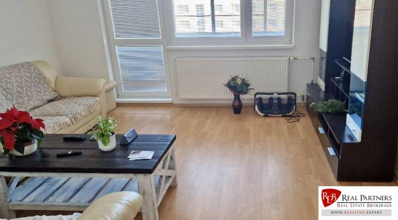 Prenájom 3 - izbový byt Bratislava - Petržalka - Obývacia izba v 3-izbovom byte s podlahou s dreveným dekorom a pohodlnou sedačkou.