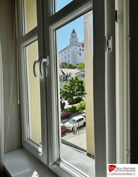 Prenájom veľkého luxusného 2izb bytu pri Bratislavskom hrade - Výhľad z 2-izbového bytu na Bratislavský hrad cez okno s bielym rámom.