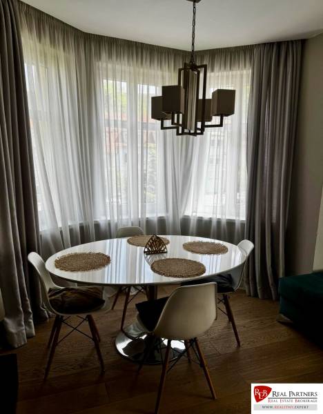 Prenájom veľkého luxusného 2izb bytu pri Bratislavskom hrade - Jedálenský kút v 2-izbovom byte s okrúhlym stolom, závesmi a podlahou s dreveným dekorom.