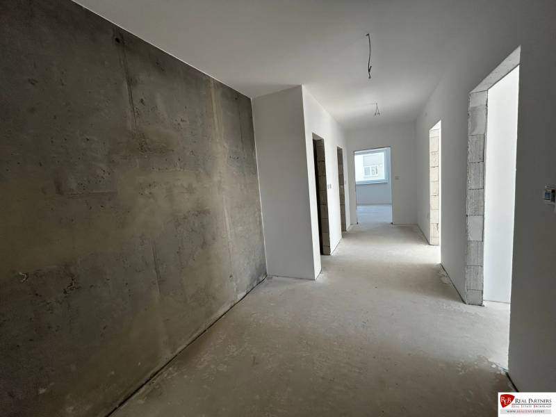 Predaj 3-izbového bytu len 15 minút od Bratislavy  - Chodba v 3-izbovom byte s hladkými stenami a odkrytým betónovým múrom.