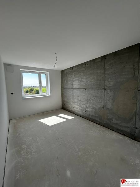Predaj 3-izbového bytu len 15 minút od Bratislavy  - Svetlá izba s betónovou stenou a oknom v 3-izbovom byte.