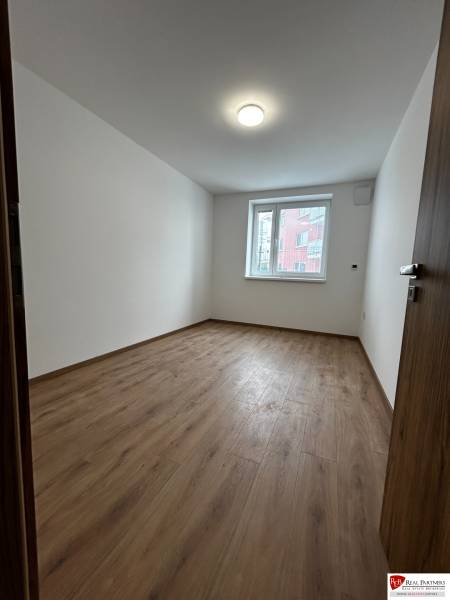 3-izbový byt v štandarde vrátane kuchyne len 15 minút od BA - Prázdna izba v 4-izbovom byte s podlahou s dreveným dekorom a bielymi stenami.