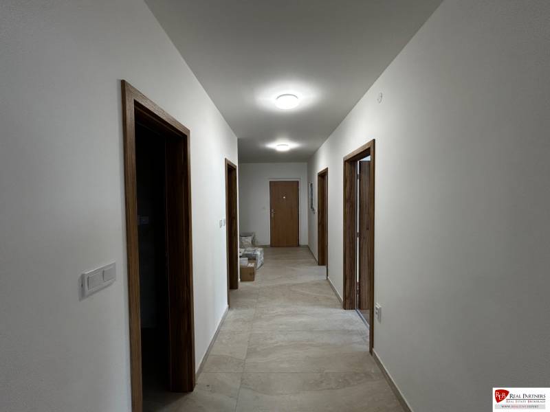 3-izbový byt v štandarde vrátane kuchyne len 15 minút od BA - Chodba v 4-izbovom byte s dlažbou a drevenými zárubňami, osvetlená stropnými svietidlami.