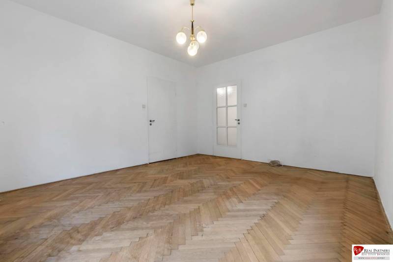 Predaj 4-izbový byt, 102m2, terasa 50m2, Bratislava-centrum, Gorkého - Priestranná miestnosť s bielymi stenami a podlahou s dreveným dekorom v 4-izbovom byte.