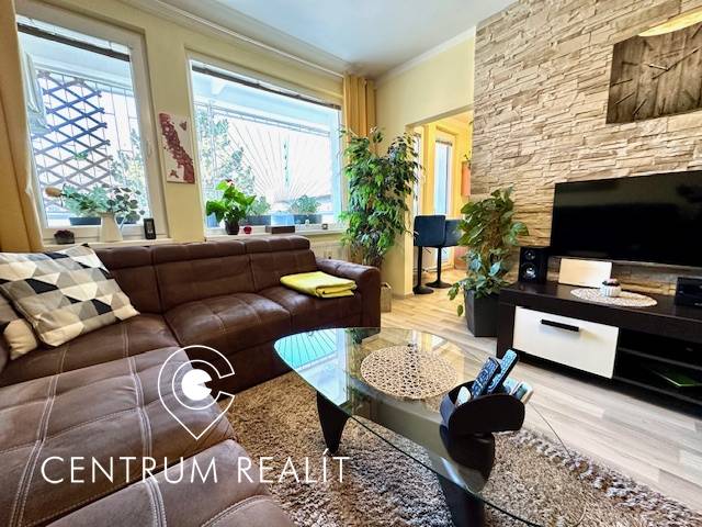 1 izb. zrekonštruovaný byt s veľkou loggiou, Karlova Ves - Obývačka v 1-izbovom byte s hnedou sedačkou a podlahou s dreveným dekorom.