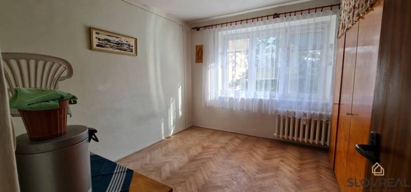 Na predaj 3i byt Levice, 61m2 - Izba s oknom a podlahou s dreveným dekorom v 3-izbovom byte.