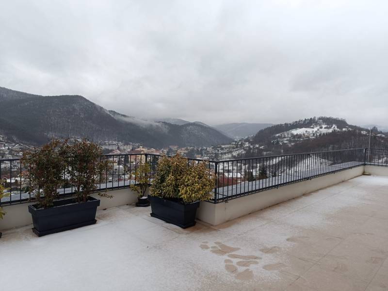 Štýlový 2-izbový byt s exkluzívnou terasou 102 m²  - Zimný výhľad na zasnežené kopce v meste Nová Baňa z balkóna v 2-izbovom byte.