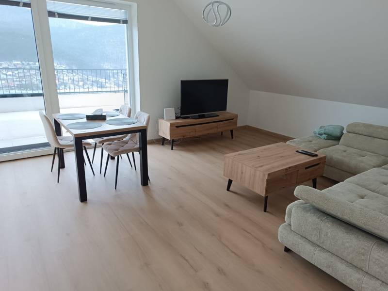 Štýlový 2-izbový byt s exkluzívnou terasou 102 m²  - Obývacia izba v 2-izbovom byte s podlahou s dreveným dekorom, jedálenským stolom a pohovkou.