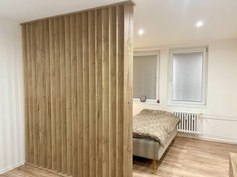 | Predaj 1-izbového bytu – Račianska, Bratislava - Spálňa s deliacou drevenou stenou a podlahou s dreveným dekorom v 1-izbovom byte.