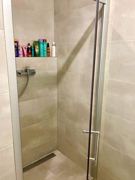 | Predaj 1-izbového bytu – Račianska, Bratislava - Sprchový kút v 1-izbovom byte so šampónmi a kozmetikou na poličke.