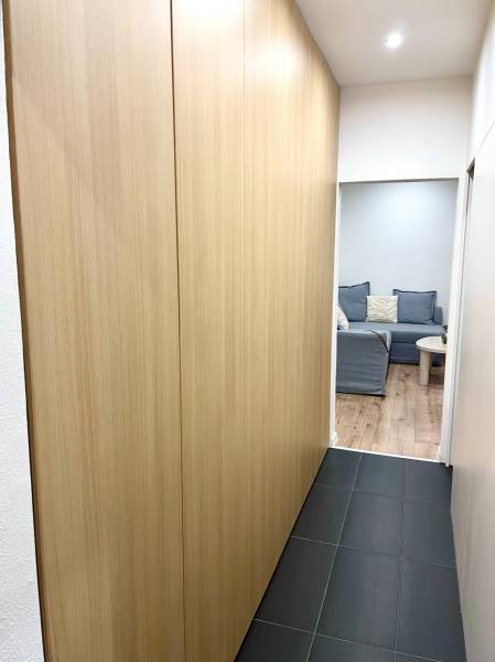 | Predaj 1-izbového bytu – Račianska, Bratislava - Chodba s tmavou podlahou, vstavanými skriňami a výhľadom do obývačky v 1-izbovom byte.