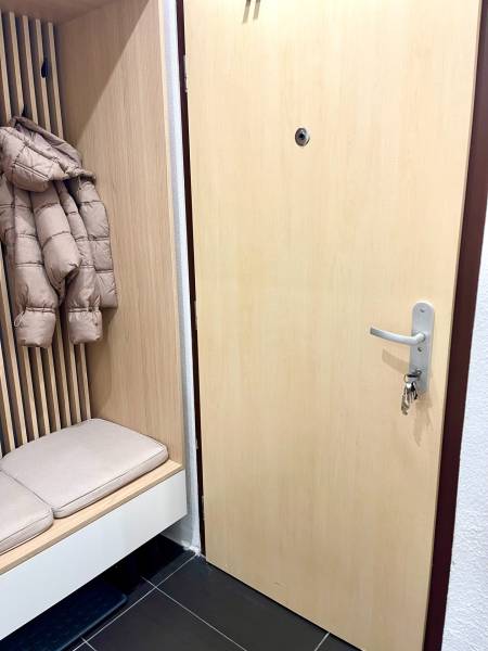 | Predaj 1-izbového bytu – Račianska, Bratislava - Vstupná chodba s lavicou, vešiakmi a svetlými dverami v 1-izbovom byte.