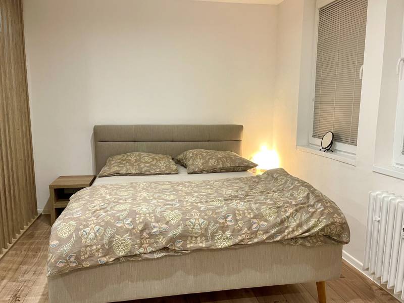 | Predaj 1-izbového bytu – Račianska, Bratislava - Spálňa v 1-izbovom byte s manželskou posteľou a podlahou s dreveným dekorom.