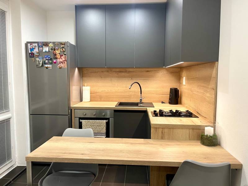 | Predaj 1-izbového bytu – Račianska, Bratislava - Kuchyňa v 1-izbovom byte s tmavými skrinkami a dreveným dekorom na doskách.