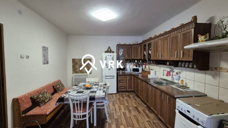 3 IZBOVÝ RODINNÝ DOM S GARÁŽOU, VEĽKÉ OZOROVCE - Kuchyňa v rodinnom dome s drevenými skrinkami a podlahou s dreveným dekorom.