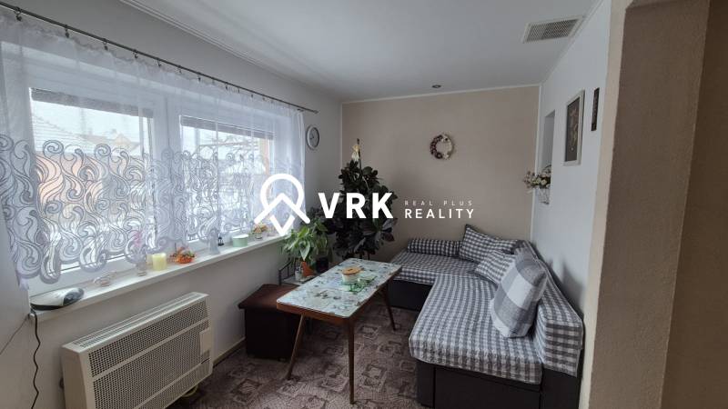 3 IZBOVÝ RODINNÝ DOM S GARÁŽOU, VEĽKÉ OZOROVCE - Obývacia izba v rodinnom dome s gaučom, stolom a oknom so záclonou.