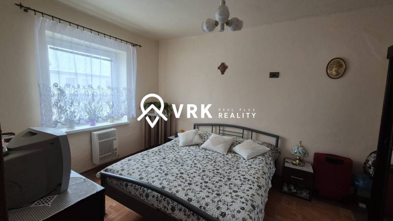 3 IZBOVÝ RODINNÝ DOM S GARÁŽOU, VEĽKÉ OZOROVCE - Spálňa v rodinnom dome so vzorovaným prehozom, televíziou a podlahou s dreveným dekorom.