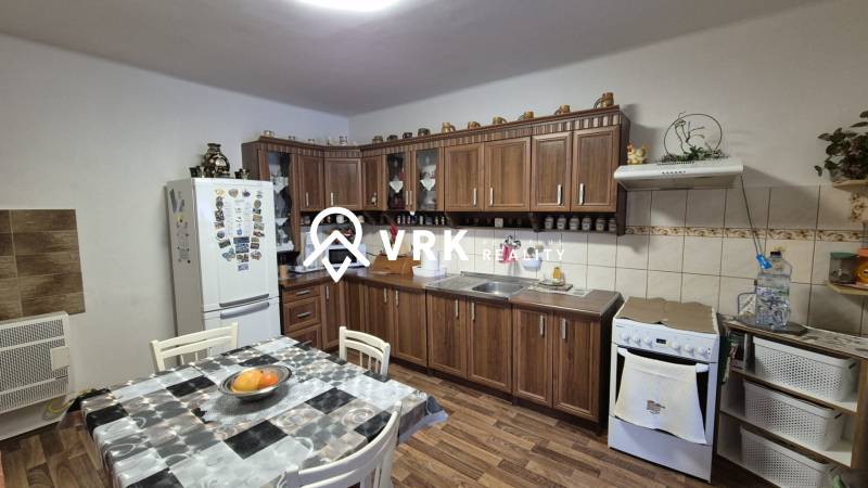 3 IZBOVÝ RODINNÝ DOM S GARÁŽOU, VEĽKÉ OZOROVCE - Kuchyňa v rodinnom dome s kuchynskou linkou, jedálenským stolom a podlahou s dreveným dekorom.