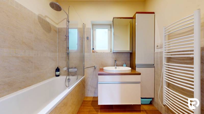 4i byt s atmosférou domu, terasou a parkovaním | Vrakuňa, 129m2 - Kúpeľňa so svetlými obkladmi, vaňou a umývadlom s podlhou s dreveným dekorom.