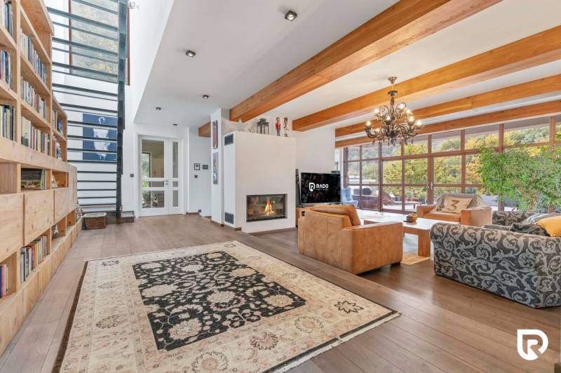 Nadštandardná 6-izbová vila v prominentnej lokalite - Interiér vily s krbom a knižnicou, doplnený o veľké okná a drevené trámy.