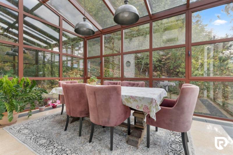 Nadštandardná 6-izbová vila v prominentnej lokalite - Jedáleň vo Vile s presklenými stenami, ružové kreslá, stôl a kvetinové aranžmány.