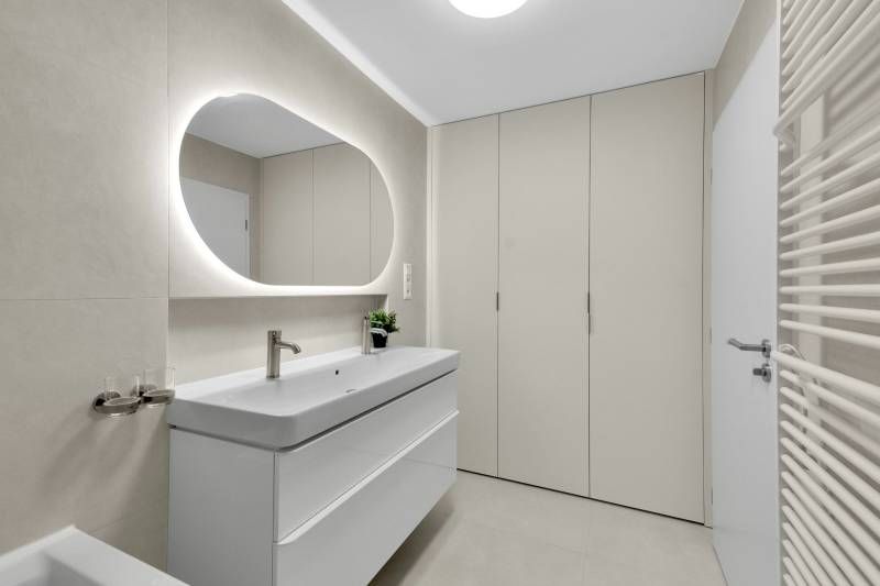 I Na predaj zrekonštruovaný 4i byt v Ružinove, Miletičova - Kúpeľňa so svetlým umývadlom, oválnym zrkadlom a úložným priestorom v 4-izbovom byte.