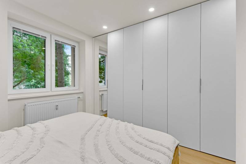 I Na predaj zrekonštruovaný 4i byt v Ružinove, Miletičova - Spálňa v 4-izbovom byte s bielymi vstavanými skriňami a podlahou s dreveným dekorom.