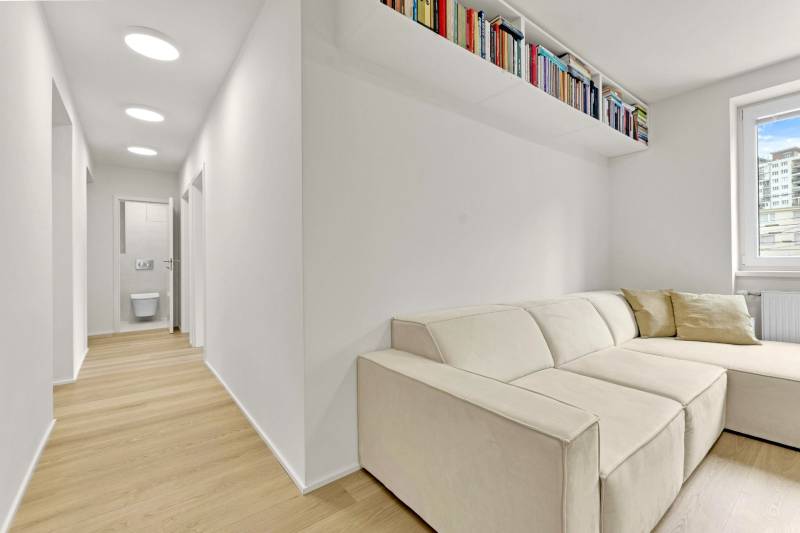 I Na predaj zrekonštruovaný 4i byt v Ružinove, Miletičova - Obývačka s krémovou sedačkou a bielou policou, podlaha s dreveným dekorom v 4-izbovom byte.