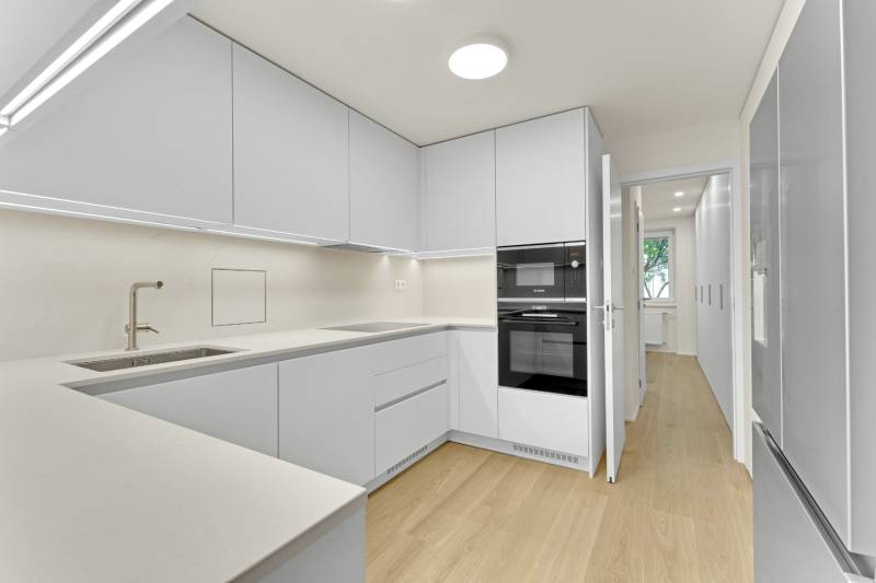 I Na predaj zrekonštruovaný 4i byt v Ružinove, Miletičova - Kuchyňa v 4-izbovom byte s bielou linkou a podlahou s dreveným dekorom.