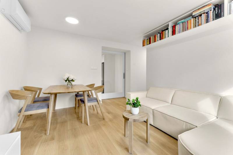 I Na predaj zrekonštruovaný 4i byt v Ružinove, Miletičova - Obývačka so svetlou sedačkou, stolom a podlahou s dreveným dekorom v 4-izbovom byte.