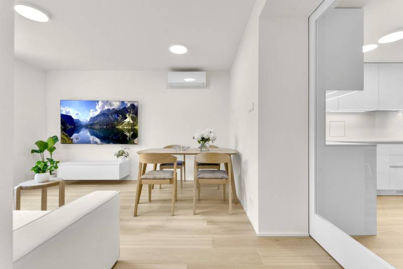 I Na predaj zrekonštruovaný 4i byt v Ružinove, Miletičova - Obývačka v 4-izbovom byte s podlahou s dreveným dekorom, televízorom a kvetmi.