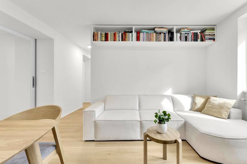 I Na predaj zrekonštruovaný 4i byt v Ružinove, Miletičova - Obývacia izba s bielou pohovkou, dreveným stolíkom a poličkou plnou kníh v 4-izbovom byte.