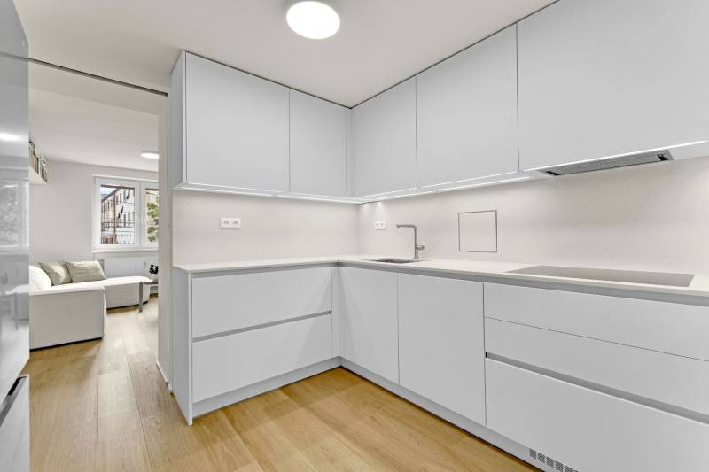 I Na predaj zrekonštruovaný 4i byt v Ružinove, Miletičova - Kuchyňa v 4-izbovom byte s bielymi skrinkami a podlahou s dreveným dekorom.